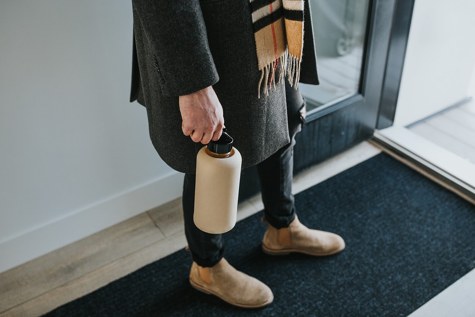 One litre glass water bottle with sand, nude protective silicone sleeve. Lifestyle photography of man holding bottle, with grey coat and Burberry scarf - lifewithPandJ
